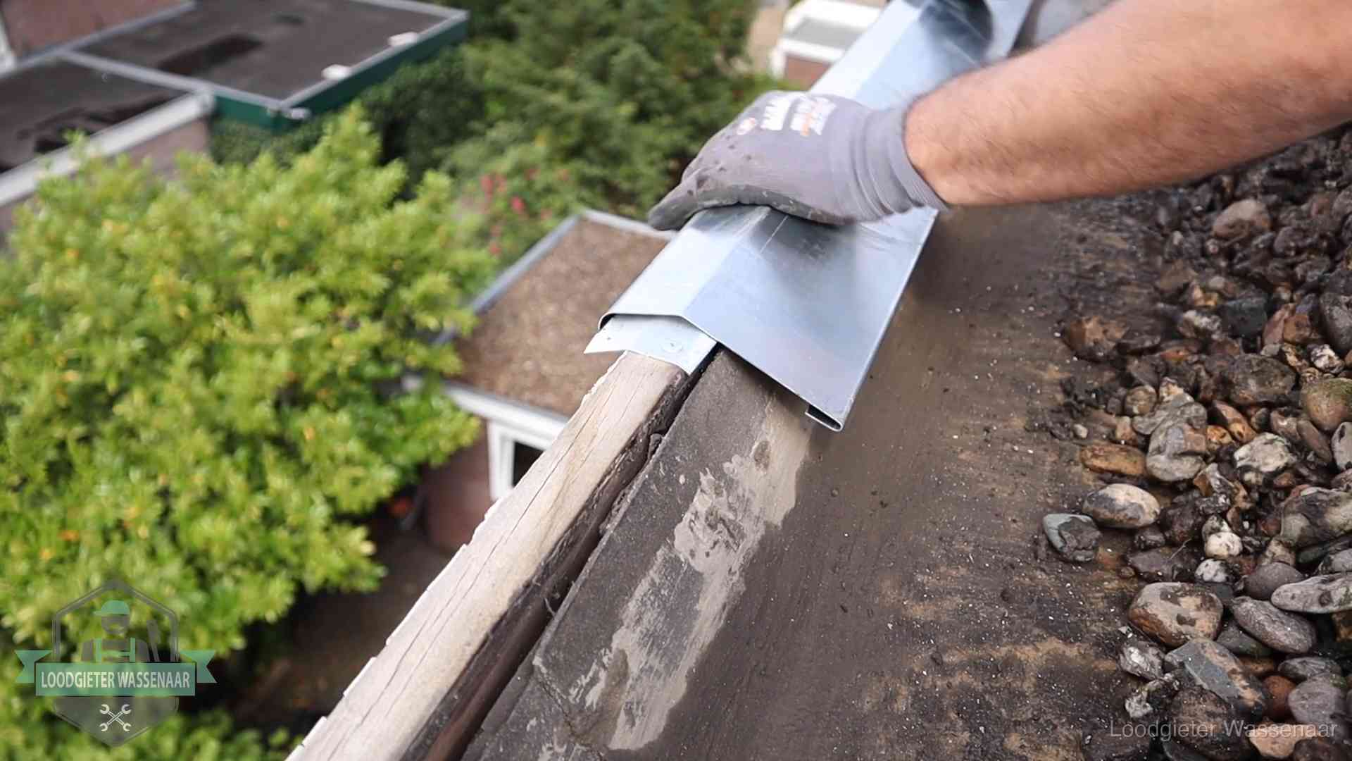 Daklekkage per wijk in Wassenaar Dakdekker plaatst een zinken deklijst op een dakrand met uitzicht over een woonwijk in Wassenaar