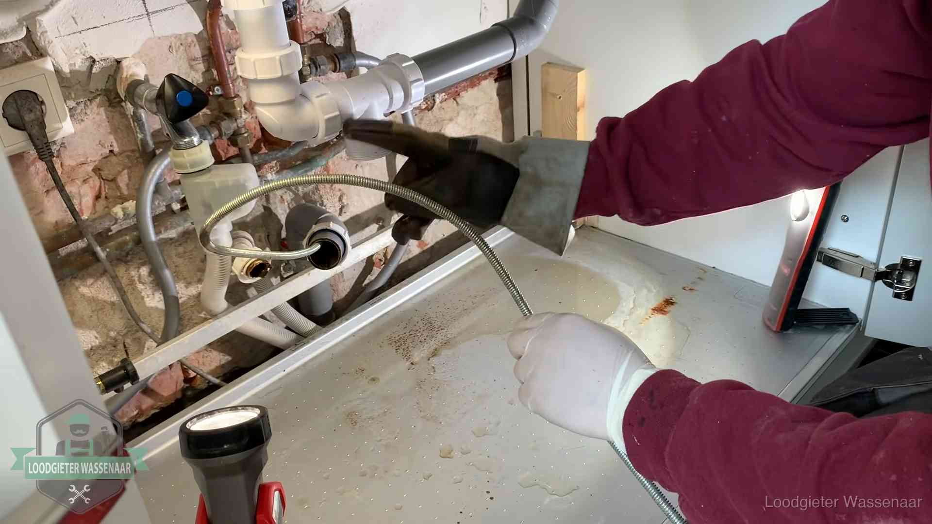 Ontstoppingsveer gaat in een geopende sifonaansluiting onder het aanrecht in Wassenaar
