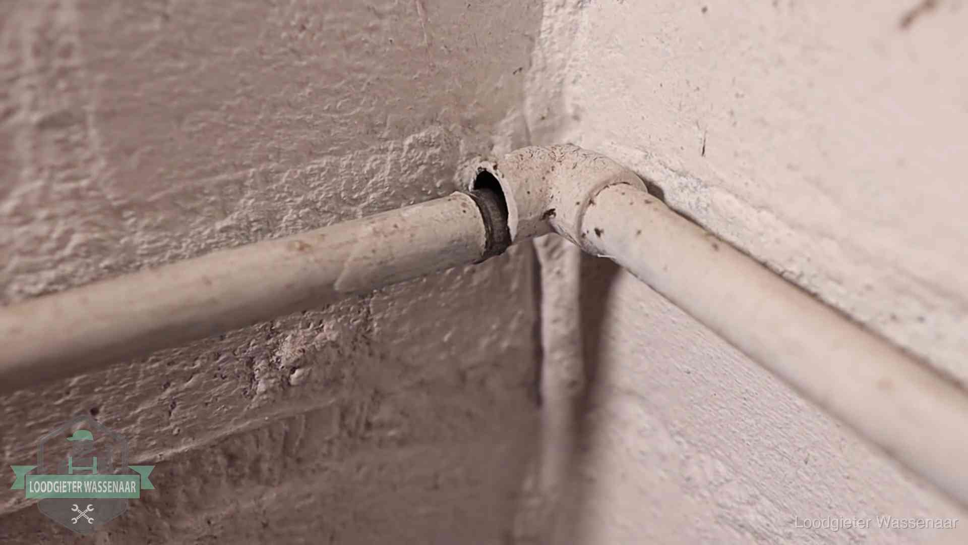 Oude geverfde waterleiding met een losliggende fitting in een woning in Wassenaar