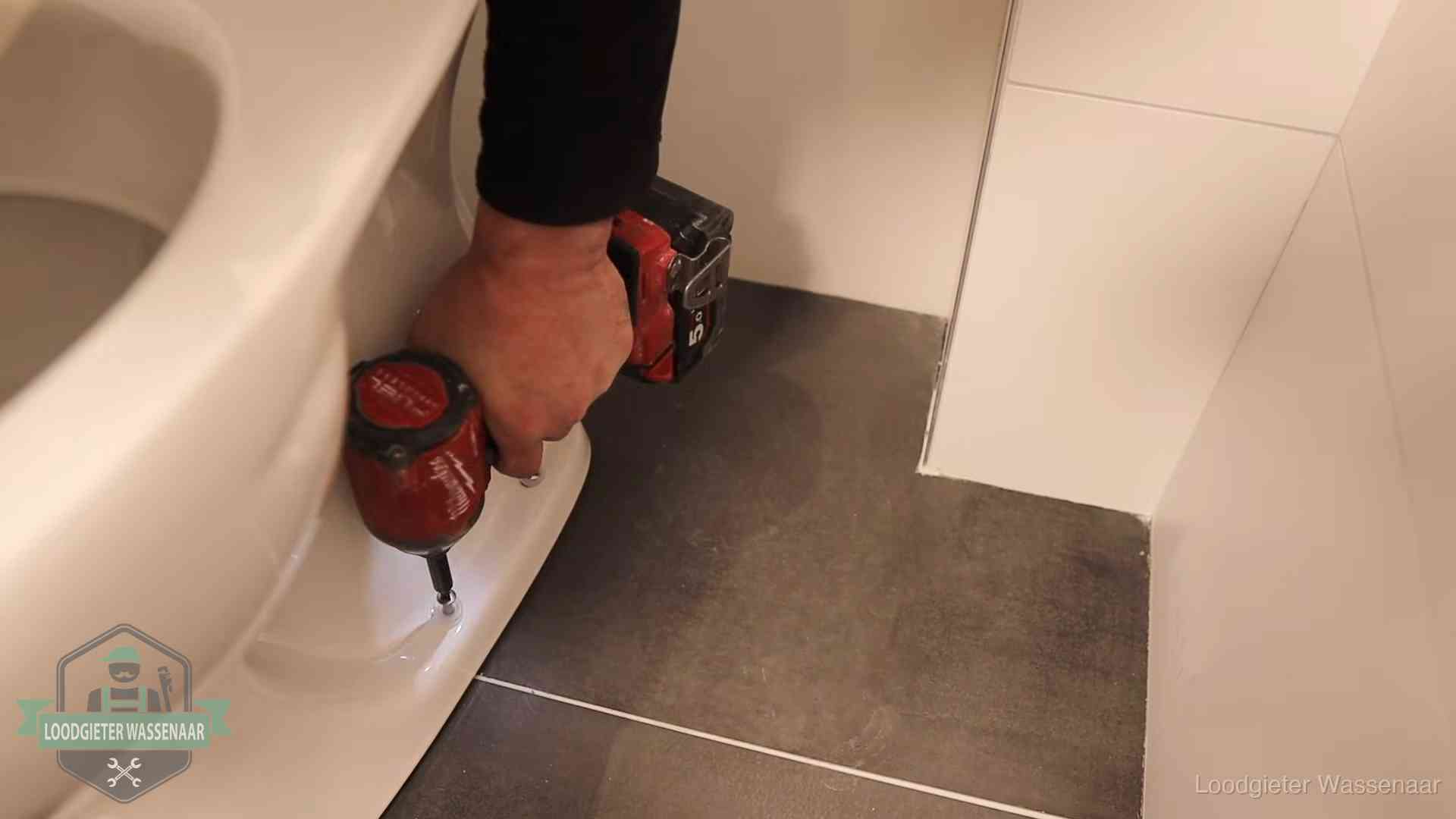 Loodgieter zet de voet van een wc-pot vast op de tegelvloer in Wassenaar